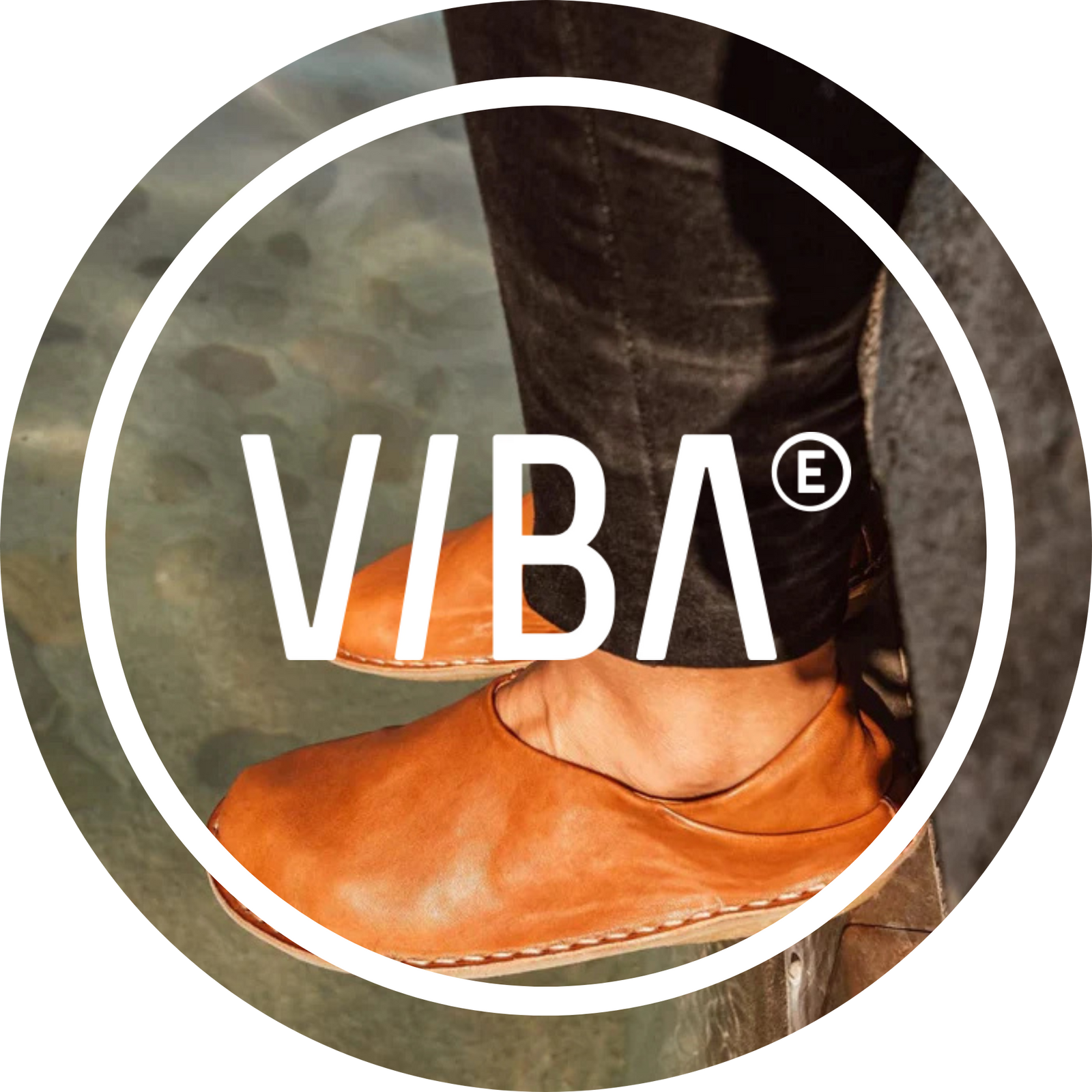 Bruna minimalistiska läderskor från märket VIBA bärs av en person vid vattnet. Logotypen VIBA syns centrerad över bilden.