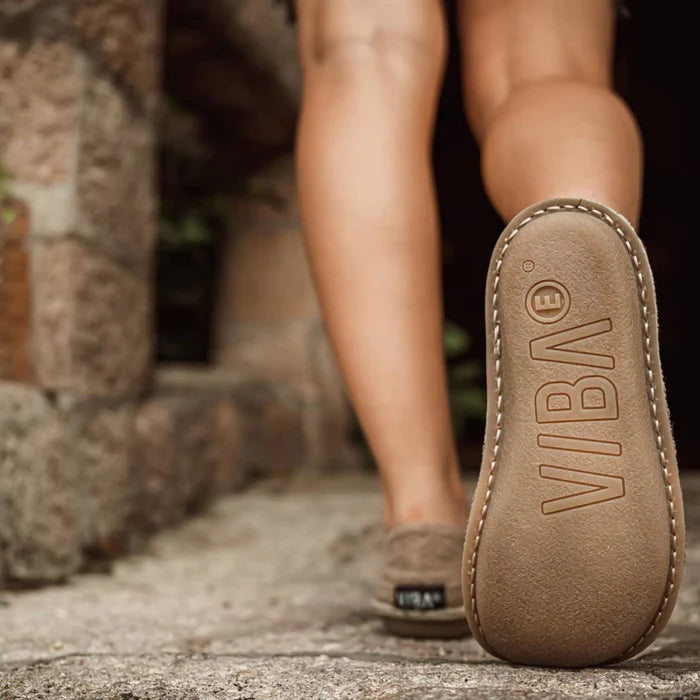 Närbild bakifrån på person som går i VIBA Zuma barfotaskor i färgen Linen Oak. Fokus på den flexibla sulan med VIBA-logotyp och handsydd sula – barfotalik känsla för naturlig rörelse.